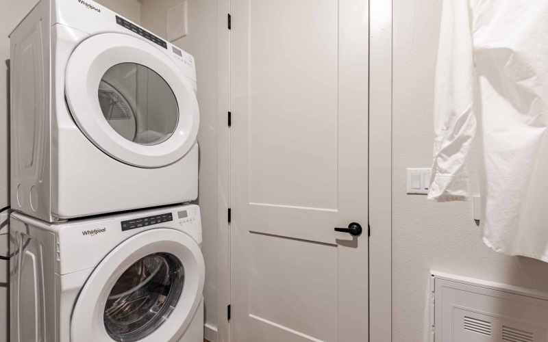 A room with a  white washer and dryer stacked on top