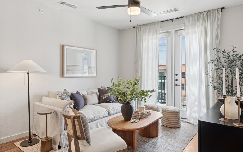 A room with a ceiling fan, seating, and tv stand